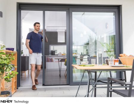 Insektenschutz. Ein Mann steht an einer Plisseetüre, die auf die Terrasse führt.